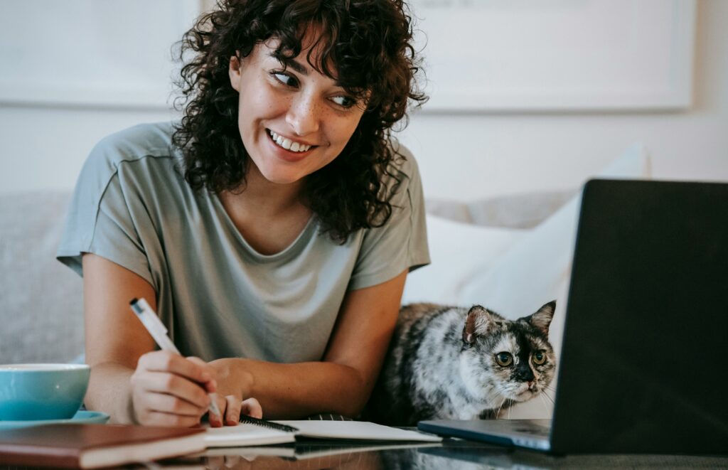 Cat is looking at the computer next to a human that is writing.