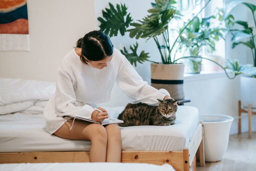 Cat being petted by a person writing something on a bed.